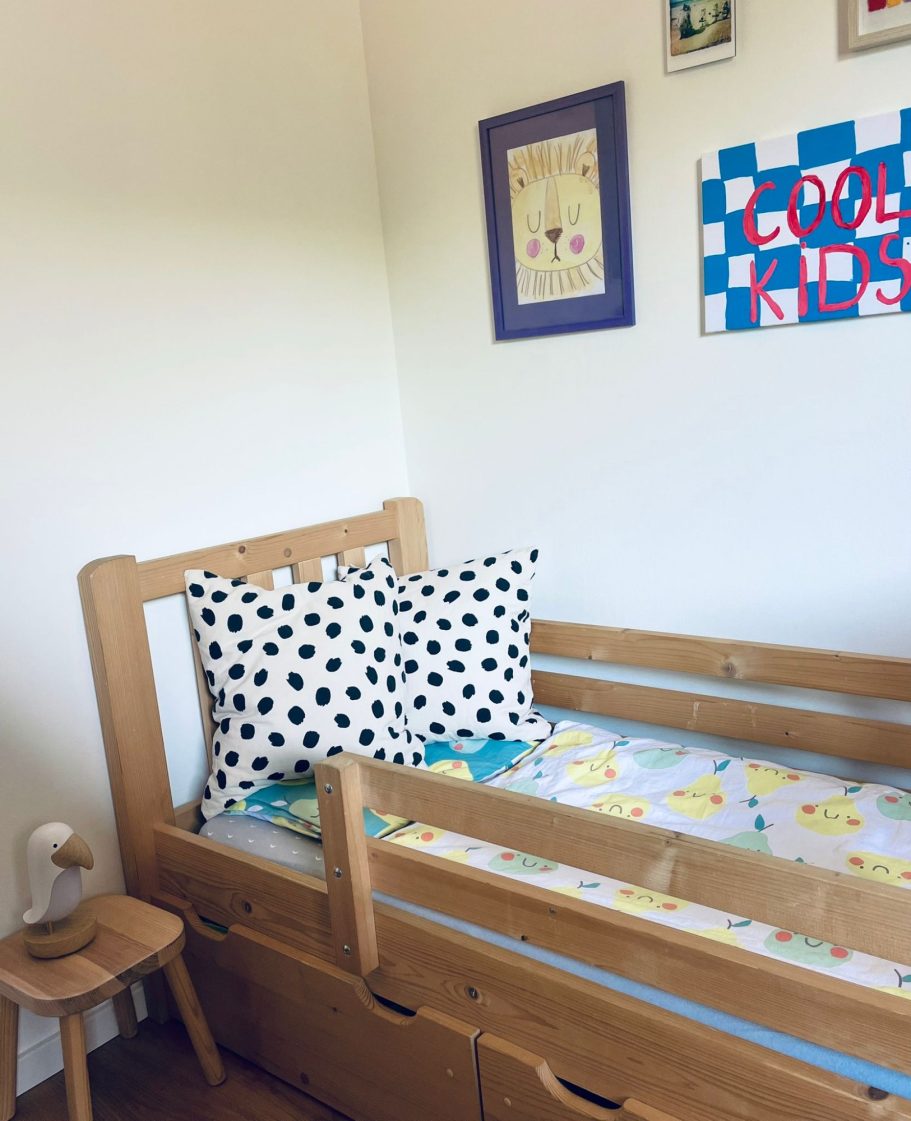 Kinderbett Schlafzimmer 2 Holzbett für Kinder mit gepunkteten Kissen und buntem Bettlaken in einem hellen Zimmer.