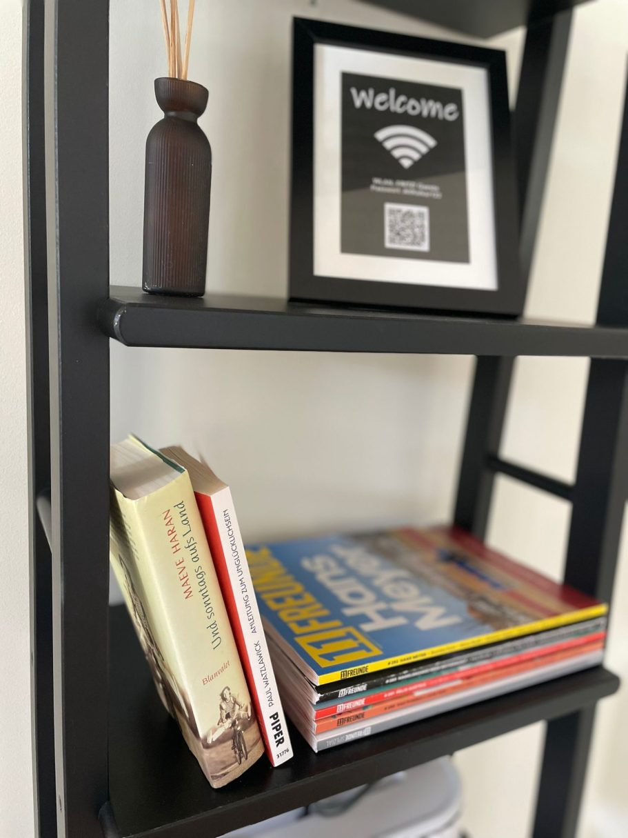Bücher Tausch Regal mit Büchern, dekorativer Vase und einem Rahmen mit WLAN-QR-Code.