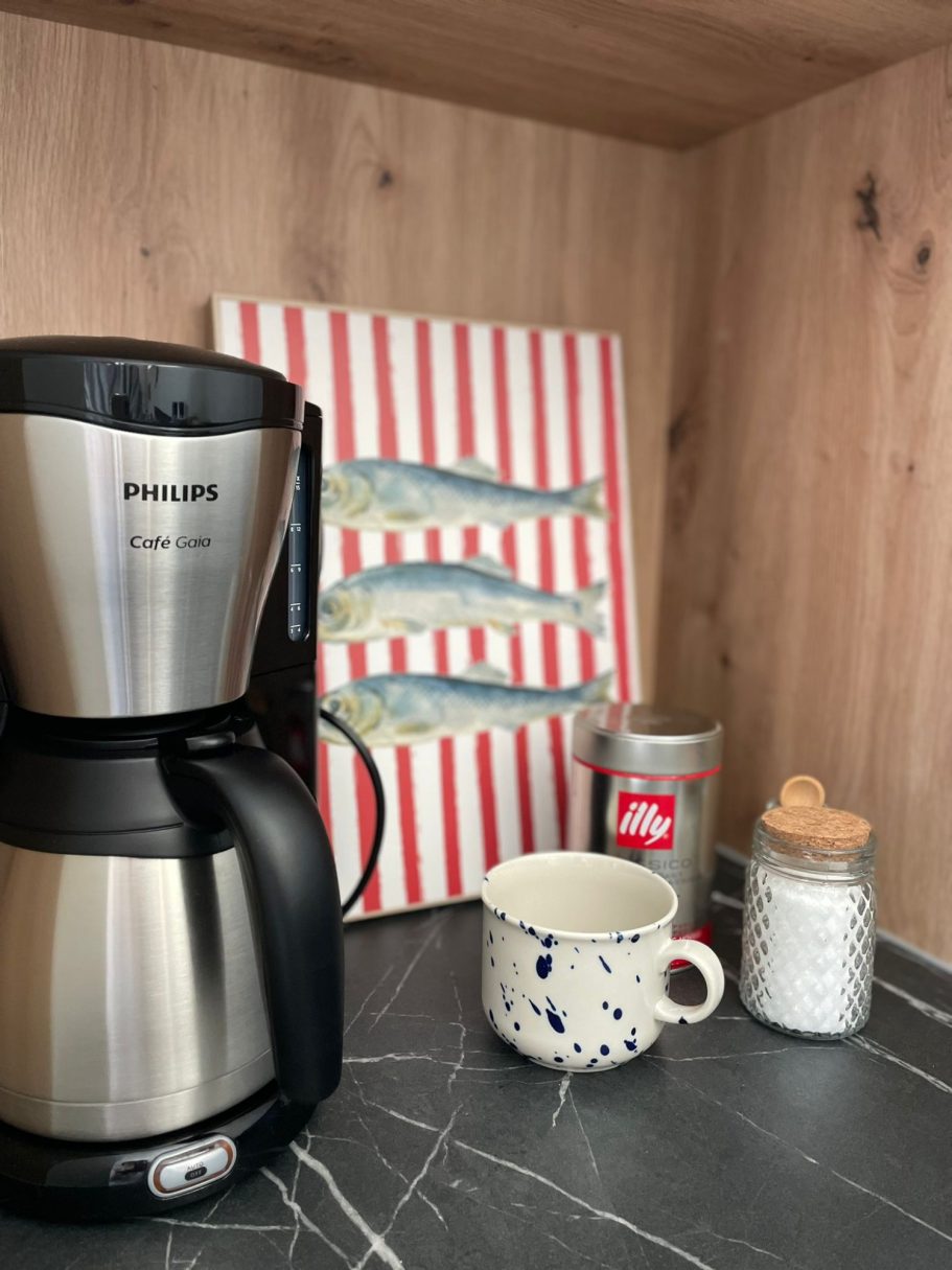Kaffee Ecke Kaffeemaschine neben einer Tasse, einem Glas und einer Zuckerdose auf einer Arbeitsfläche.