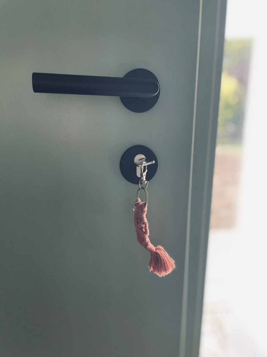 Willkommen / Welcome / Welkom Schlüssel mit pinkem Anhänger hängt an einem schwarzen Türschloss.