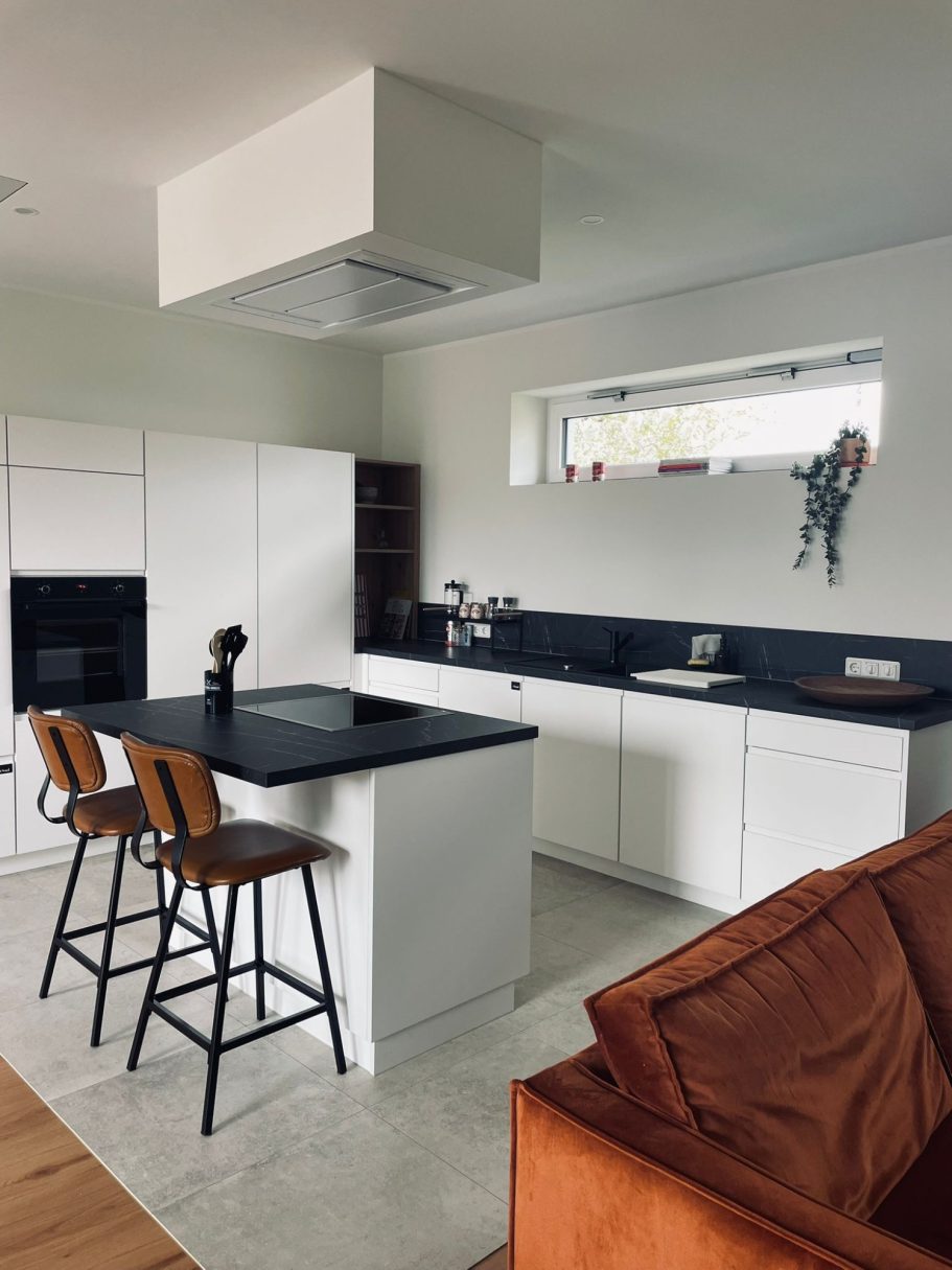 vollausgestattete Küche Moderne Küche mit weißen Schränken, schwarzem Tisch und Holzstuhl. Heller Raum mit Fenster.