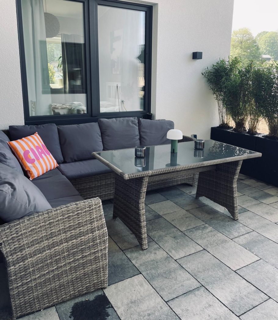 überdachte Terasse Gemütliche Terrasse mit einem Sitzsofa, Glastisch und grünen Pflanzen im Hintergrund.