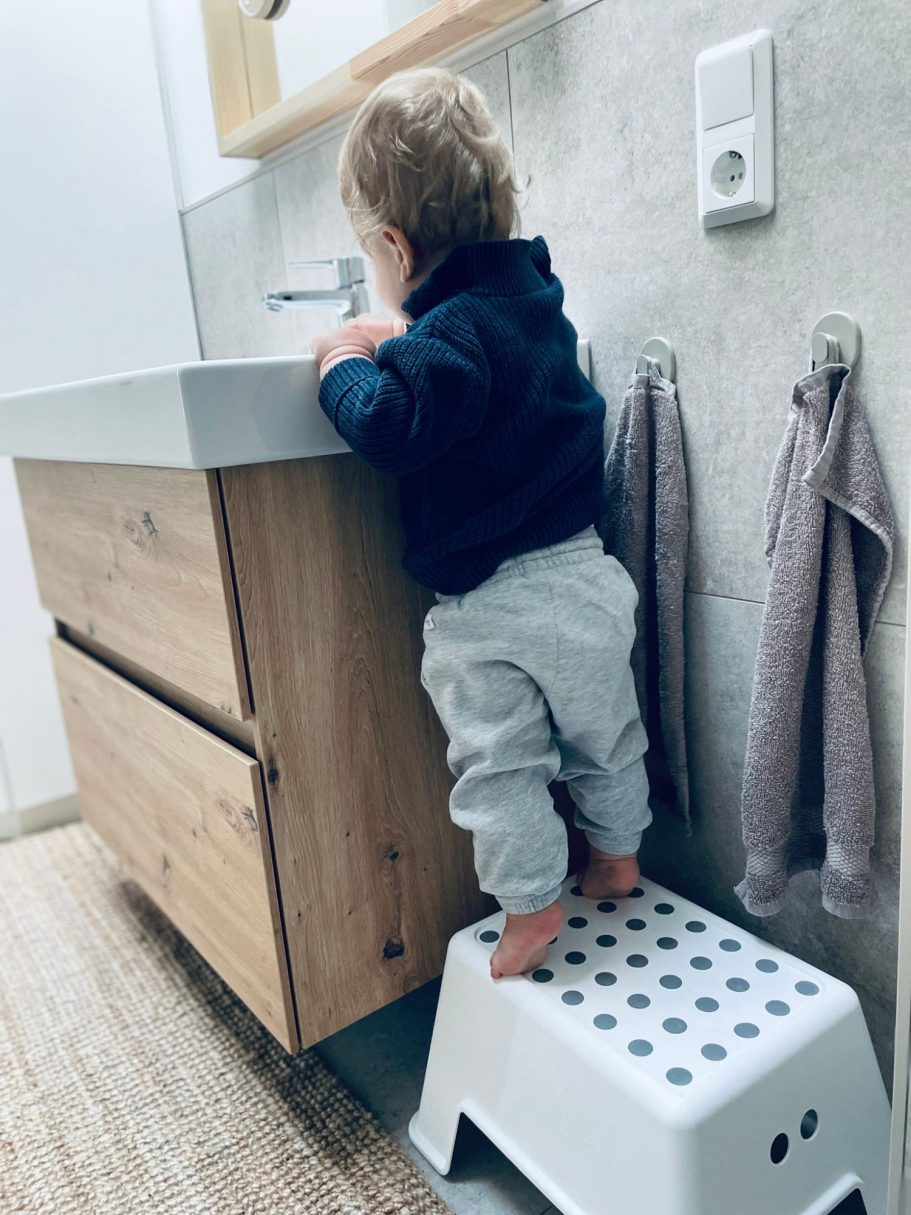 kinderfreundliche Details Ein kleines Kind steht auf einem Hocker vor einem Badezimmerwaschbecken.